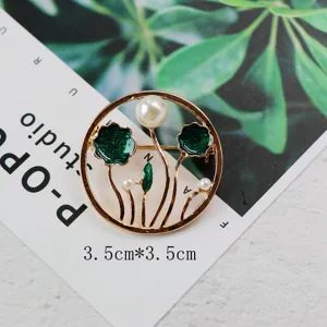 Close-up of vintage golden brooch with green enamel leaves and pearls.