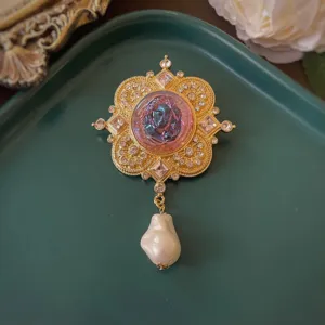 Primo piano di una spilla barocca dorata con cammeo iridescente e perla barocca
