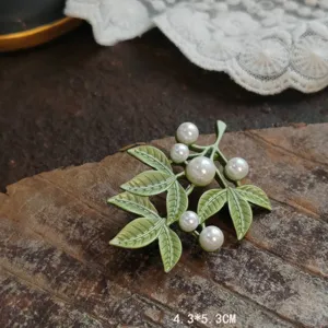 Macro view of vintage green enamel leaf brooch with delicate white pearl clusters