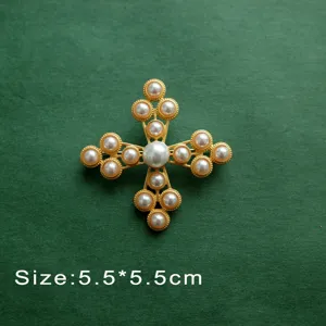 Elegant vintage baroque style cross brooch inlaid with white pearls on a green textured surface