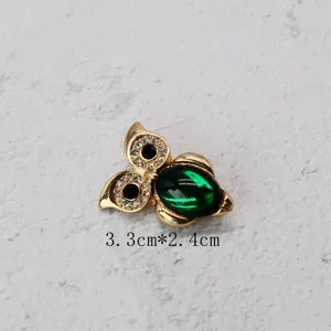 Macro view of a vintage golden owl brooch with a green oval gemstone and crystals.