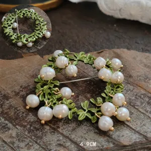 Detailed close-up of a vintage enamel lily of the valley brooch with white pearls on wood.