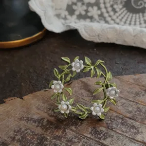 Vintage enamel leaf wreath brooch with white flowers and pearls on wood texture