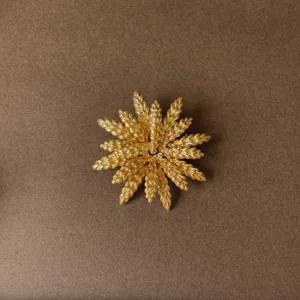 Detailed view of vintage golden sunburst brooch with a textured radial wheat design