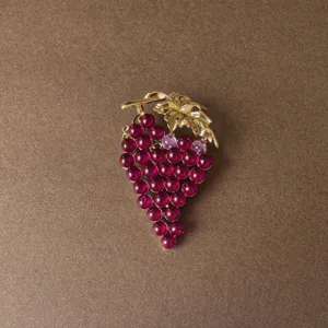 Close-up detail of a vintage Baroque style grape brooch with golden leaf and red beads