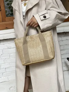 Detalle de un bolso de paja chic con base dorada y asas de lona, estilo rústico de playa.