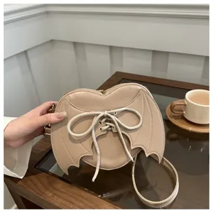 Detailopname van beige hartvormige crossbodytas met decoratieve vleermuis vleugels.