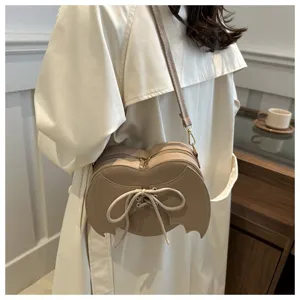 Detail van een beige hartvormige tas met duivelsvleugels en decoratieve vetersluiting