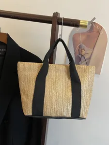 Detalle de bolso tote de paja con asas de lona negra colgado en un perchero de madera.