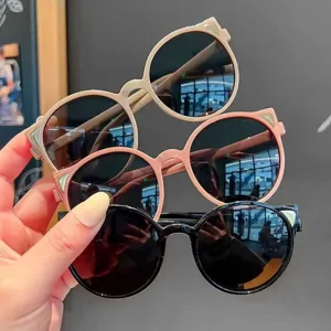 Handheld view of cute cat-ear children's sunglasses in beige, pink, and black tones