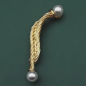 Elegante goldene Vintage-Brosche mit zwei glänzenden Perlen auf grünem Hintergrund, Detailansicht.