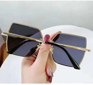 Detailansicht einer quadratischen Sonnenbrille mit dünnem Goldrahmen und dunklen Gläsern