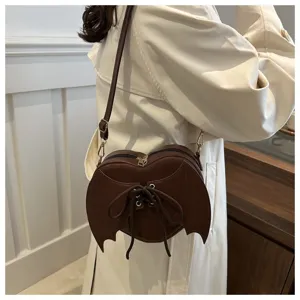 Detail van hartvormige bruine crossbodytas met vleermuisvleugels en vetersluiting