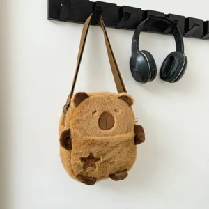 Détail du sac bandoulière en peluche Capybara marron doux suspendu sur un mur blanc
