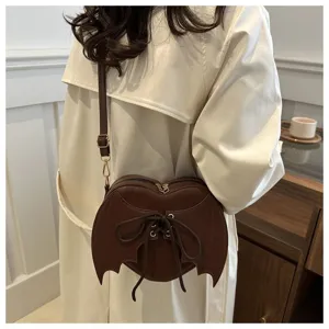 Detailweergave van bruine hartvormige duivelsvleugel crossbody tas gedragen over jas.