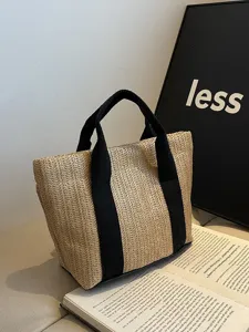 Primer plano de un bolso de paja tejido con asas negras en un entorno minimalista