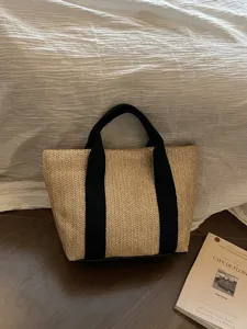 Detalle de un bolso de playa de paja tejida a mano con asas de lona negra resistentes.