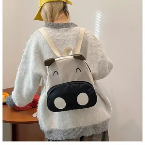 Rückansicht eines süßen Cartoon-Kuh-Rucksacks für Kinder, getragen von einer Schülerin