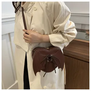 Detail van bruine hartvormige crossbodytas met vleermuisvleugels en vetersluiting.