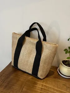 Detalle de bolso de paja tejido con asas de lona negra sobre una mesa de madera rústica