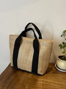 Bolso de paja tejida con asas negras sobre una superficie de madera en estilo rústico