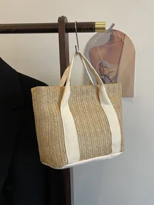 Vista detallada de un bolso de paja tejido a mano con correas de lona blanca en un colgador
