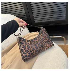 Detail of stylish leopard print underarm bag held by hand in a chic indoor setting