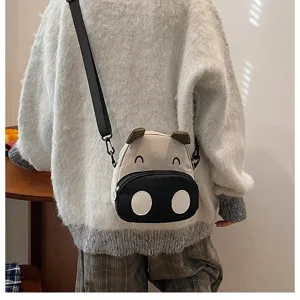 Nahaufnahme einer niedlichen Cartoon-Kuh-Tasche kombiniert mit einem weißen Pullover.