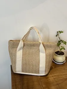 Vista detallada de la textura de paja tejida y las correas de lona blanca en un bolso.