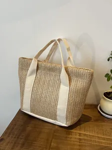 Bolso de paja natural con asas de color crema exhibido en un escritorio de madera