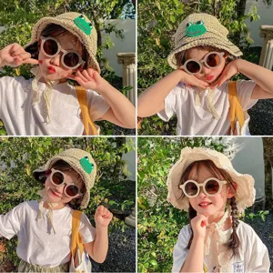 Niña con gafas de sol redondas mate UV400 y un lindo sombrero de paja con rana.