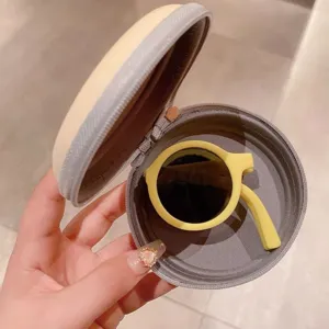 Nahaufnahme von klappbarer runder Kindersonnenbrille in einem gelben Schutzetui.