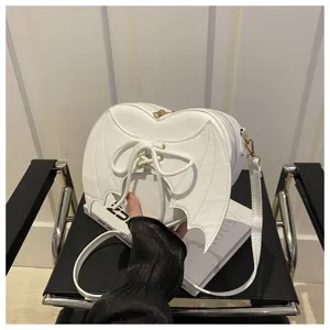 Detail van witte hartvormige crossbodytas met duivelsvleugels en vetersluiting