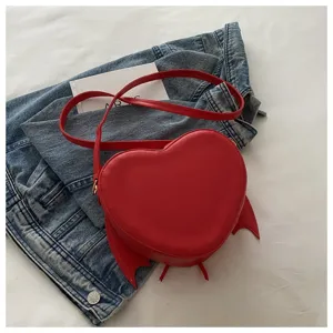 Bovenaanzicht van een rode hartvormige tas met duivelsvleugels op een denim jasje