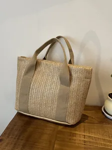 Bolso tote de paja natural tejida con asas de lona sobre una mesa de madera detalle