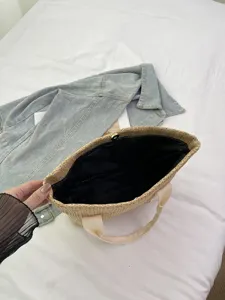 Vista detallada del interior de un bolso de paja con forro negro y cierre a presión.