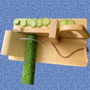 Wooden oak vegetable slicer with stainless steel blade slicing a green cucumber on blue background