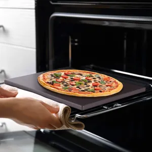 Detail view of a baking stone loaded with fresh pizza being placed inside a hot oven.