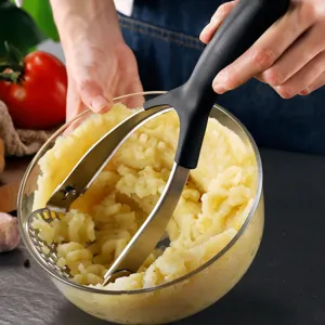 Action shot of manual stainless steel potato masher crushing boiled potatoes in a bowl