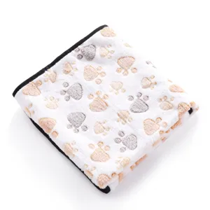 Detailed view of white fleece pet blanket featuring cute paw print pattern and black binding.