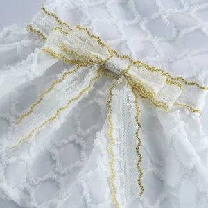 Gros plan détaillé d'une robe pour chien blanche avec nœud en dentelle et bordure dorée.
