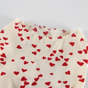 Close-up detail of cute pet dress collar with red heart print on beige fabric texture.
