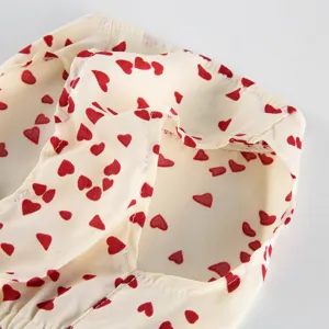Detailed close-up of pet summer dress with cute red heart print on soft cream fabric.
