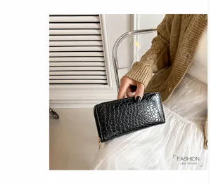 Primer plano de una cartera larga negra con relieve de cocodrilo sostenida por modelo