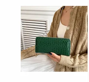 Elegante cartera larga verde con patrón de cocodrilo para mujer sostenida por modelo.