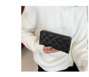 Close-up of a black quilted long wallet held by a woman in a white cardigan.