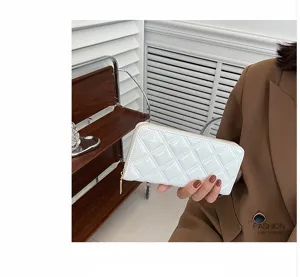 Detailed view of a white quilted patent leather long wallet held by a model