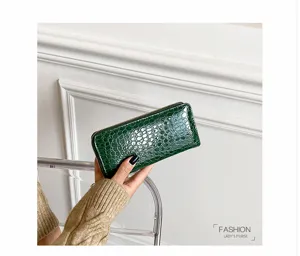 Detalle de una cartera larga verde oscuro con textura de cocodrilo brillante y cremallera