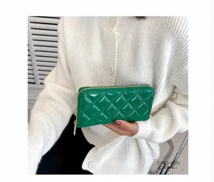 Elegant green patent leather long wallet with diamond quilted design held by model.