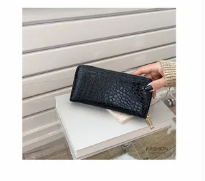 Detalle de una cartera larga para mujer negra con relieve de cocodrilo y cremallera
